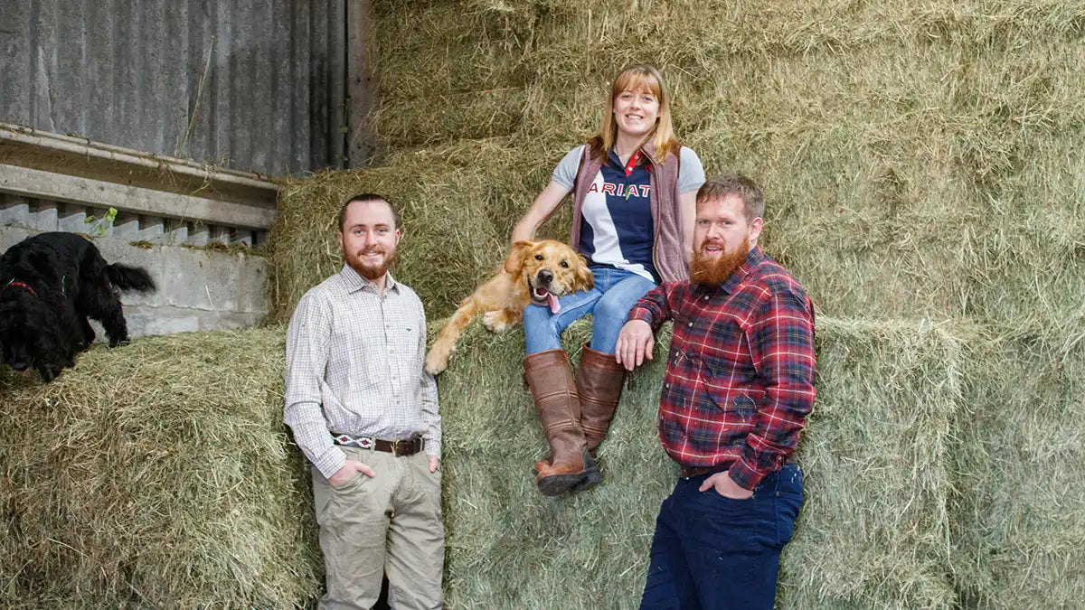 Matt, Sarah and Rob Holland leaning next to a pile of hay.