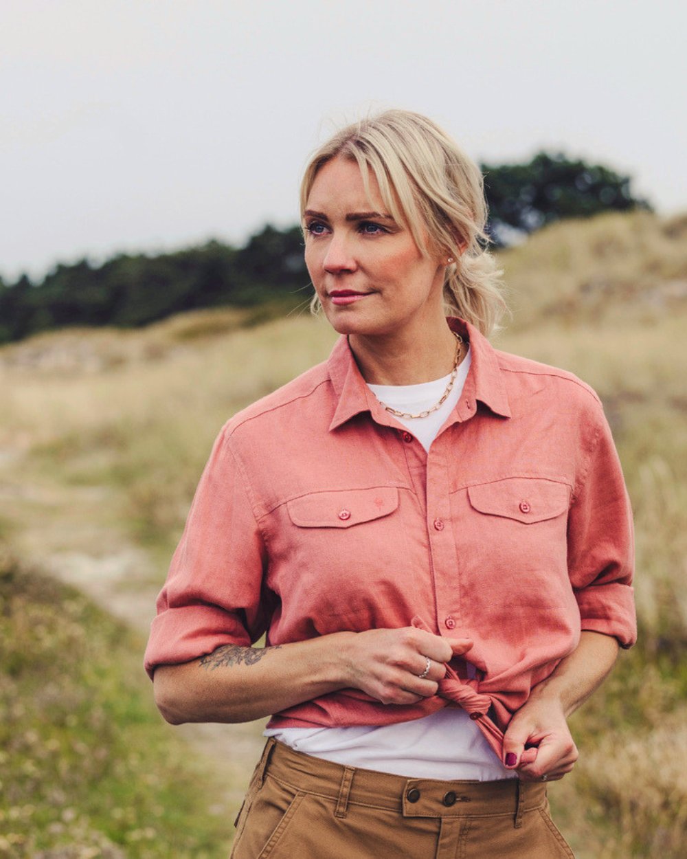 Female model stood in a field wearing a coral Pinewood shirt and white t-shirt.