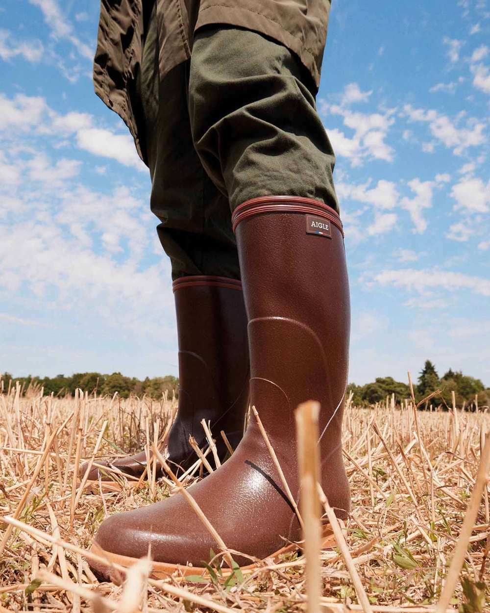 Maroon coloured Aigle Mens Tancar Pro Kevlar Reinforced Wellingtons on grassy background