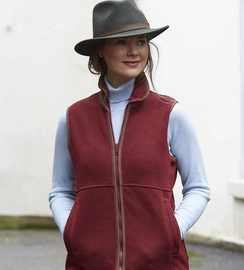 Woman wearing fleece country gilet with brown trim and felt hat over a pale blue sweater.