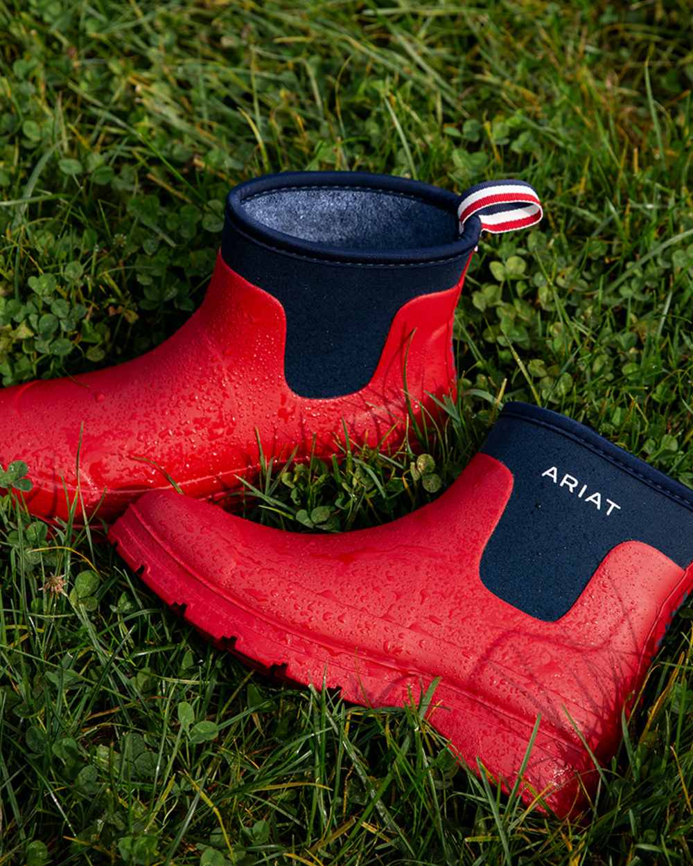 Team Red coloured Ariat Womens Kelmarsh Shortie Rubber Boots on grass background
