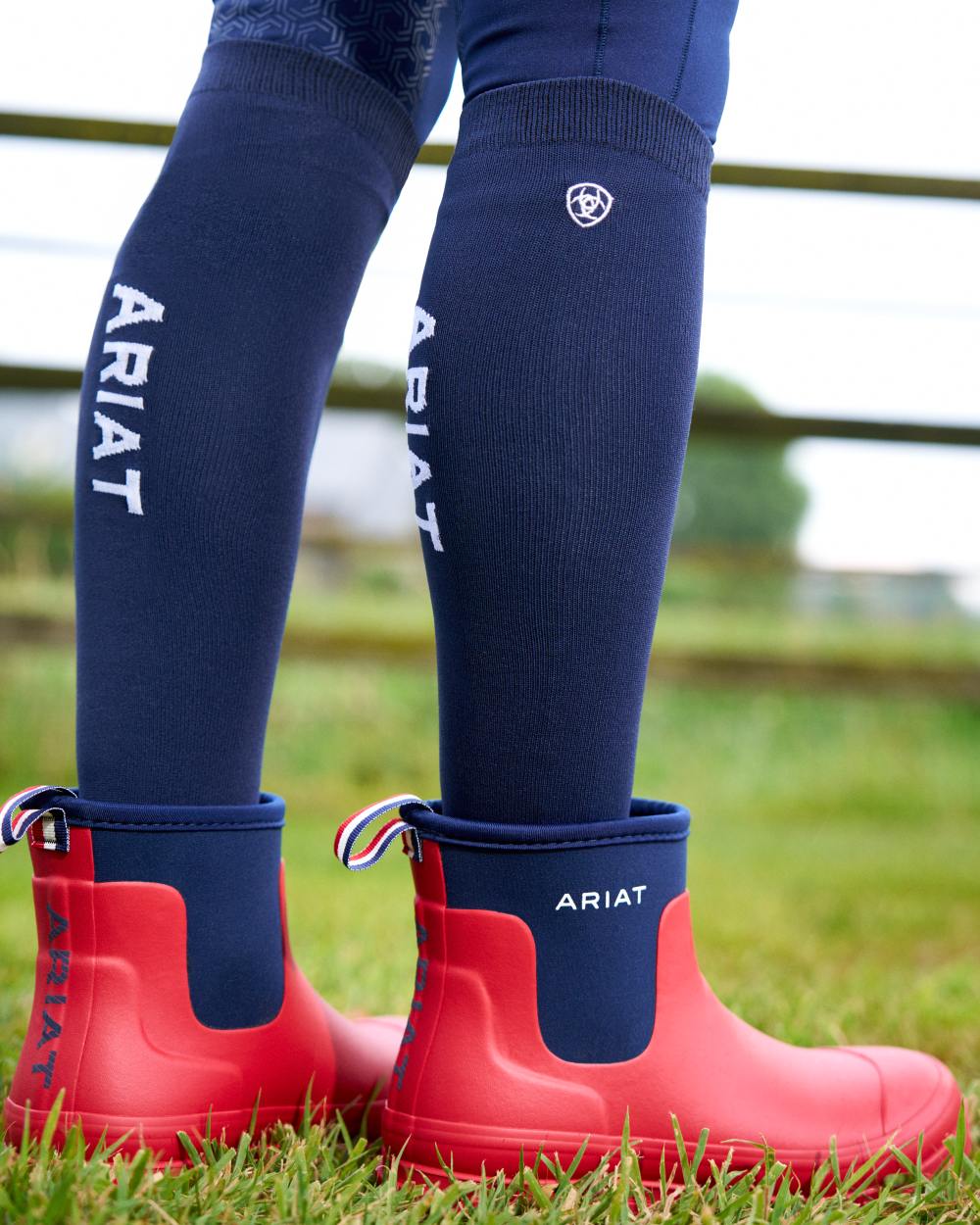 Team Red coloured Ariat Womens Kelmarsh Shortie Rubber Boots on grass background