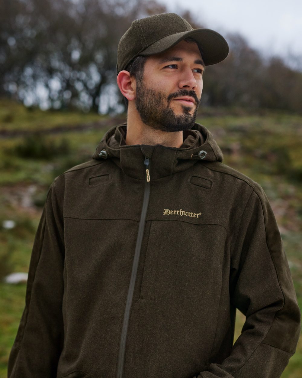 Loden Wood Coloured Deerhunter Tatra Cap With Earflaps On A Forest Background