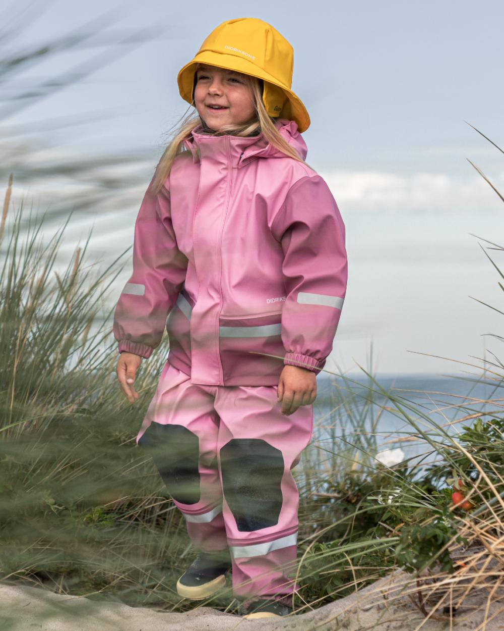 Light Heather Pink coloured Didriksons Boardman Kids Rain Set on sea background