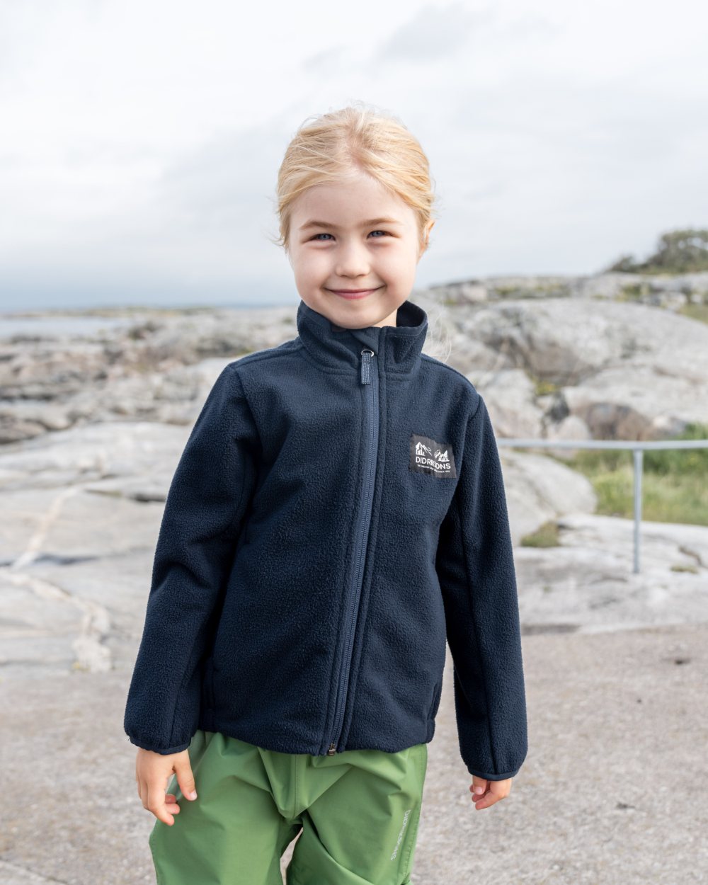 Dark Night Blue coloured Didriksons Childrens Muskot Jacket on coastal background