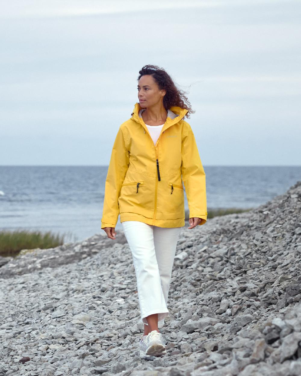Warm Yellow coloured Didriksons Womens Turvi Jacket 2 on coastal background