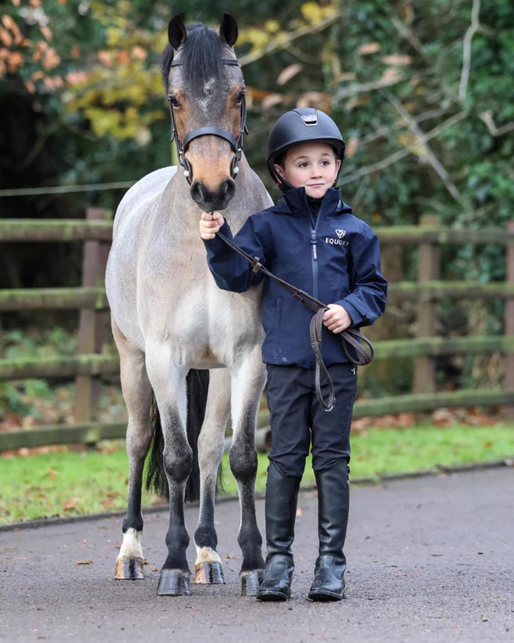 Navy coloured Equidry Childrens Nimbus Pack Away Jacket With Stowaway Hood on outdoor background