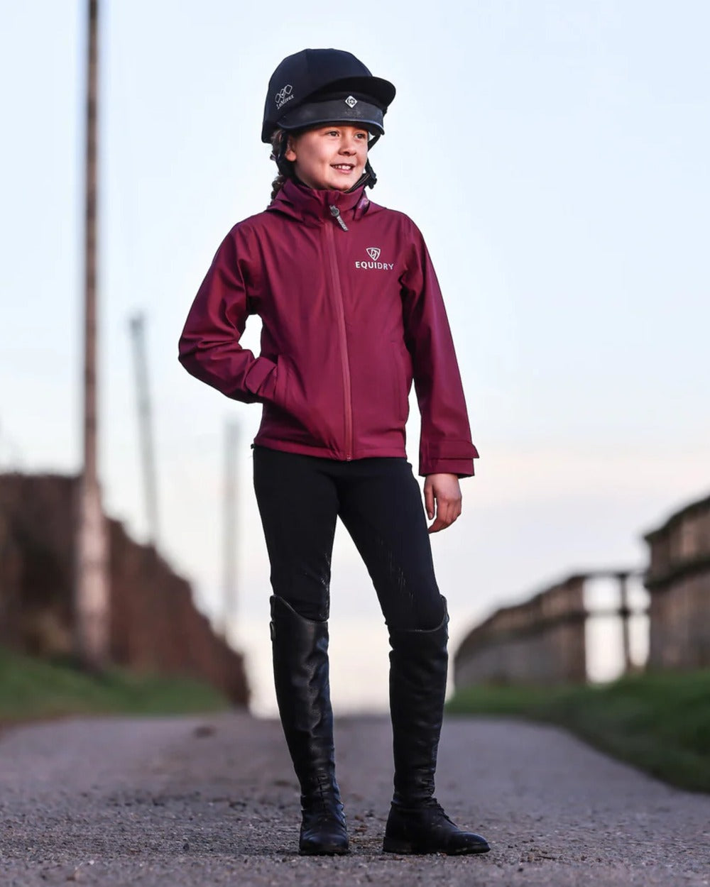 Plum coloured Equidry Childrens Nimbus Pack Away Jacket With Stowaway Hood on outdoor background
