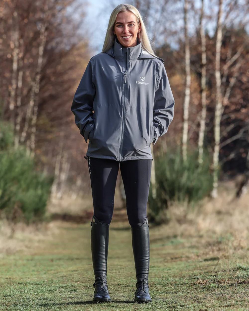 Charcoal coloured Equidry Womens Nimbus Pack Away Jacket with Stowaway Hood on forest background