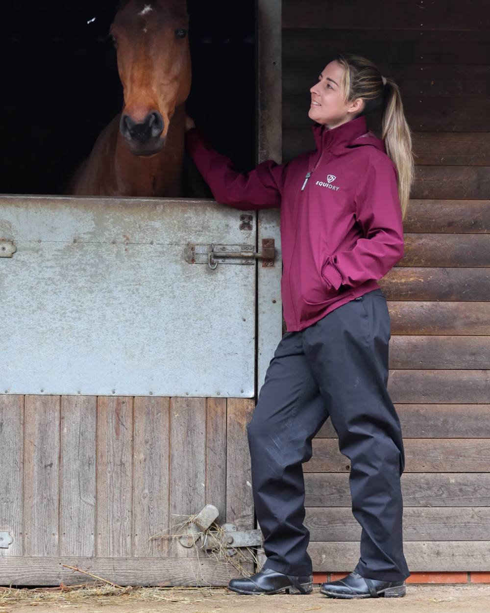 Plum coloured Equidry Womens Nimbus Pack Away Jacket with Stowaway Hood on stable background