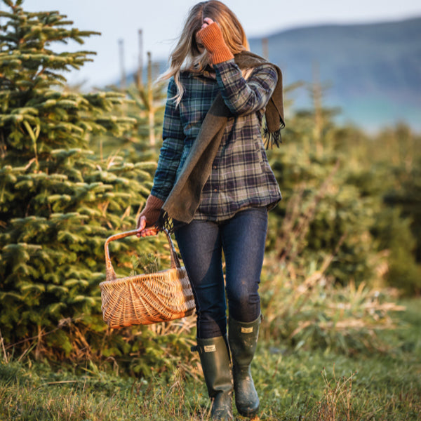 Woman walking through a Christmas tree farm holding a basket.