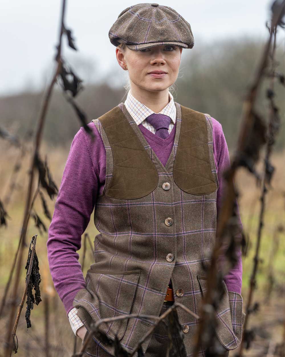 Woman wearing Laksen Pippa Beauly Tweed Shooting Vest with shoulder patches. Trees in background.