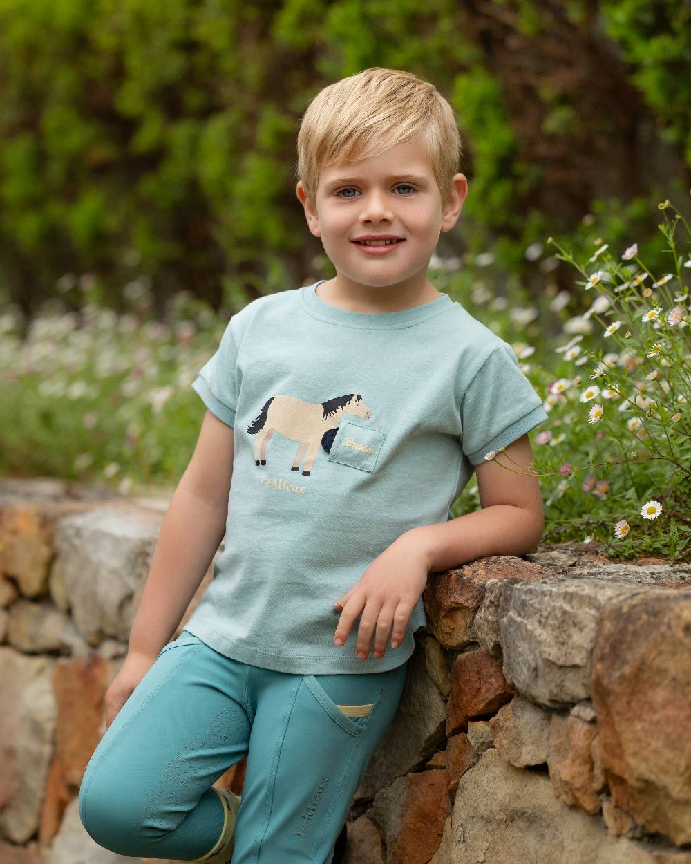 Aqua coloured LeMieux Childrens Mini Alex Tee on backyard background