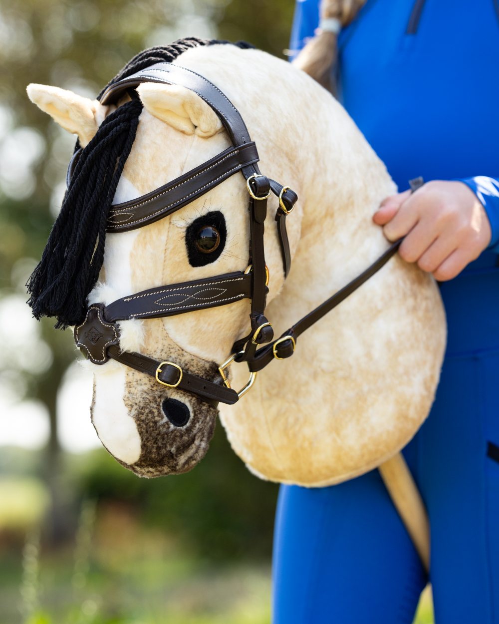 Brown coloured LeMieux Hobby Horse Grackle Bridle on tree background