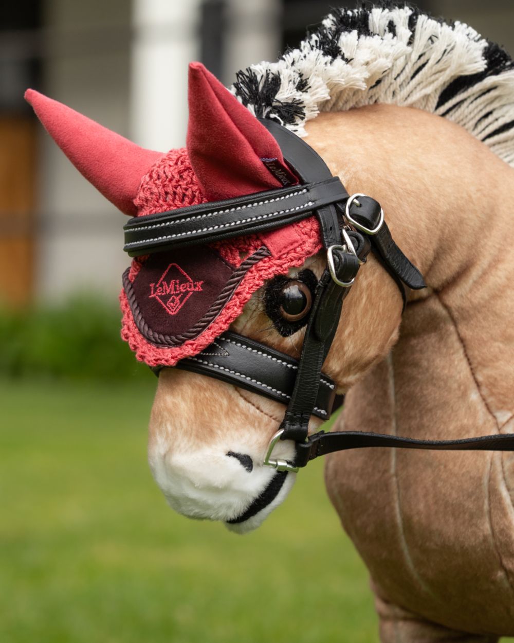 Cranberry coloured LeMieux Toy Pony Fly Hood on grassy background