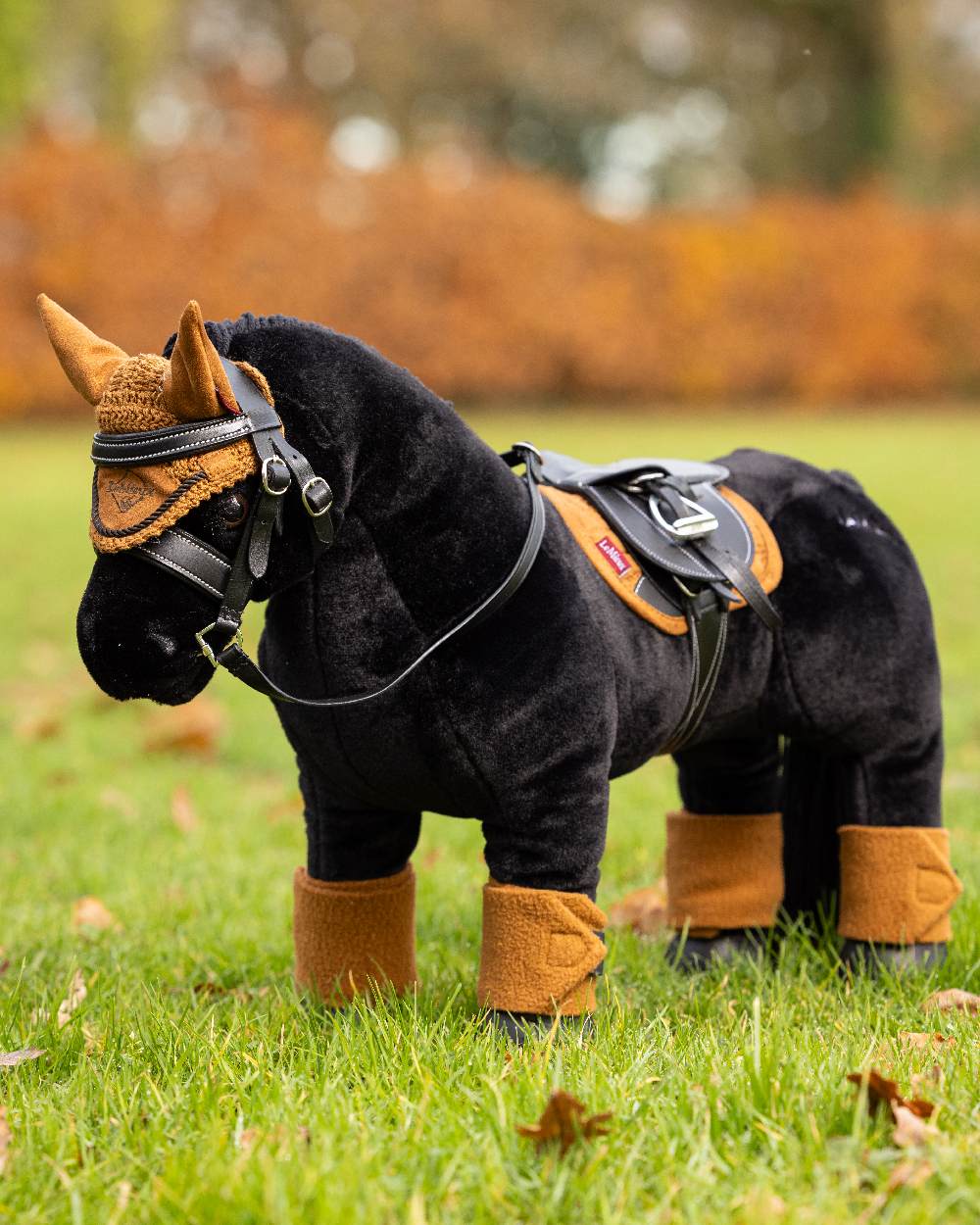Ginger coloured LeMieux Toy Pony Fly Hood on blurry grass background