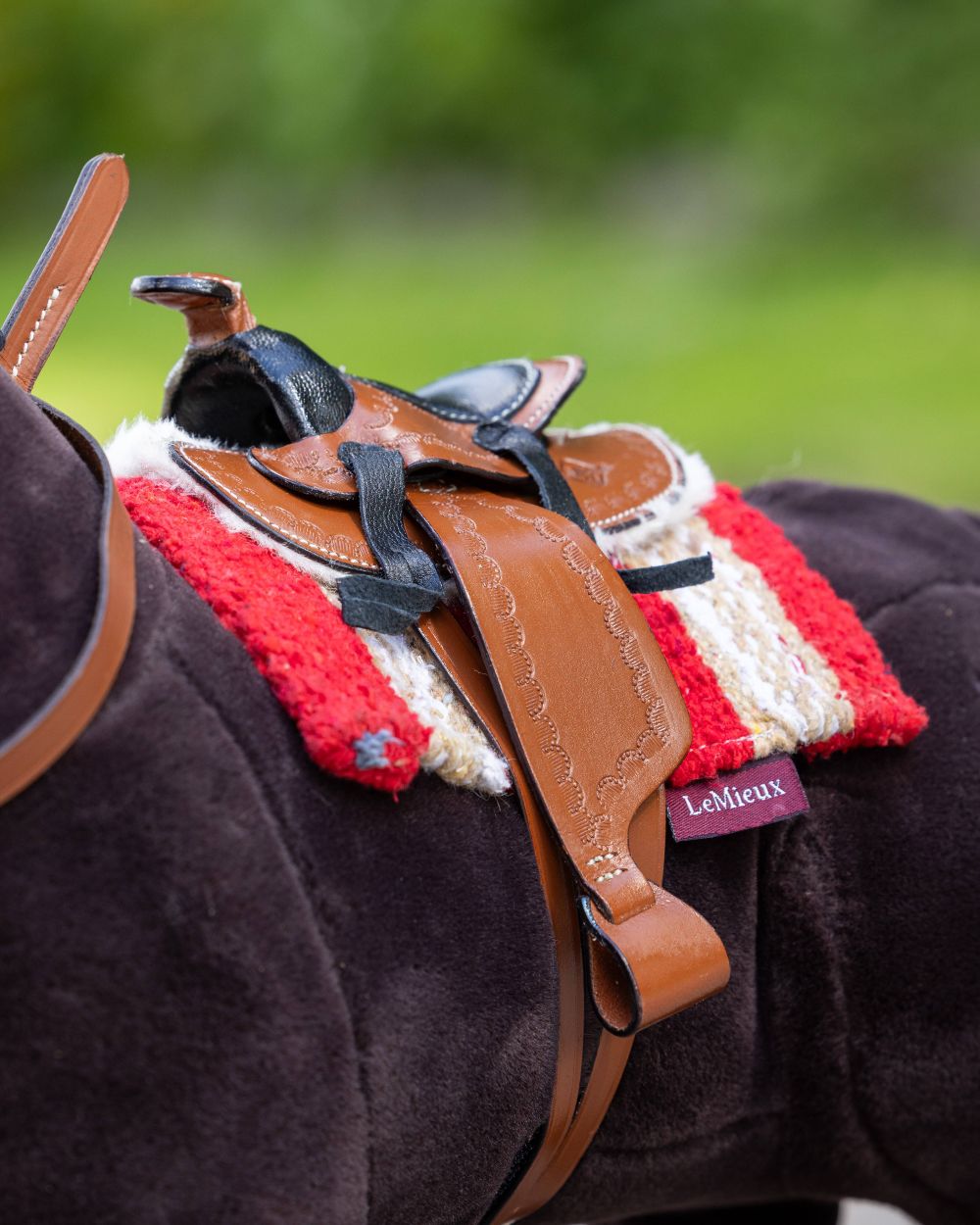 Tan coloured LeMieux Toy Pony Western Saddle on blurry green background