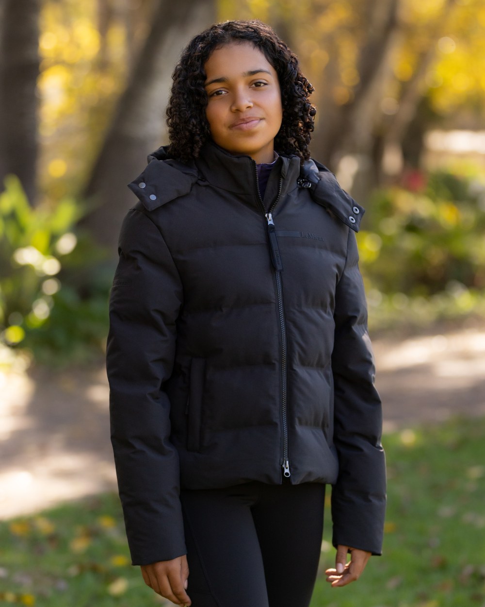 Black coloured LeMieux Young Rider Daisy Waterproof Coat on garden background