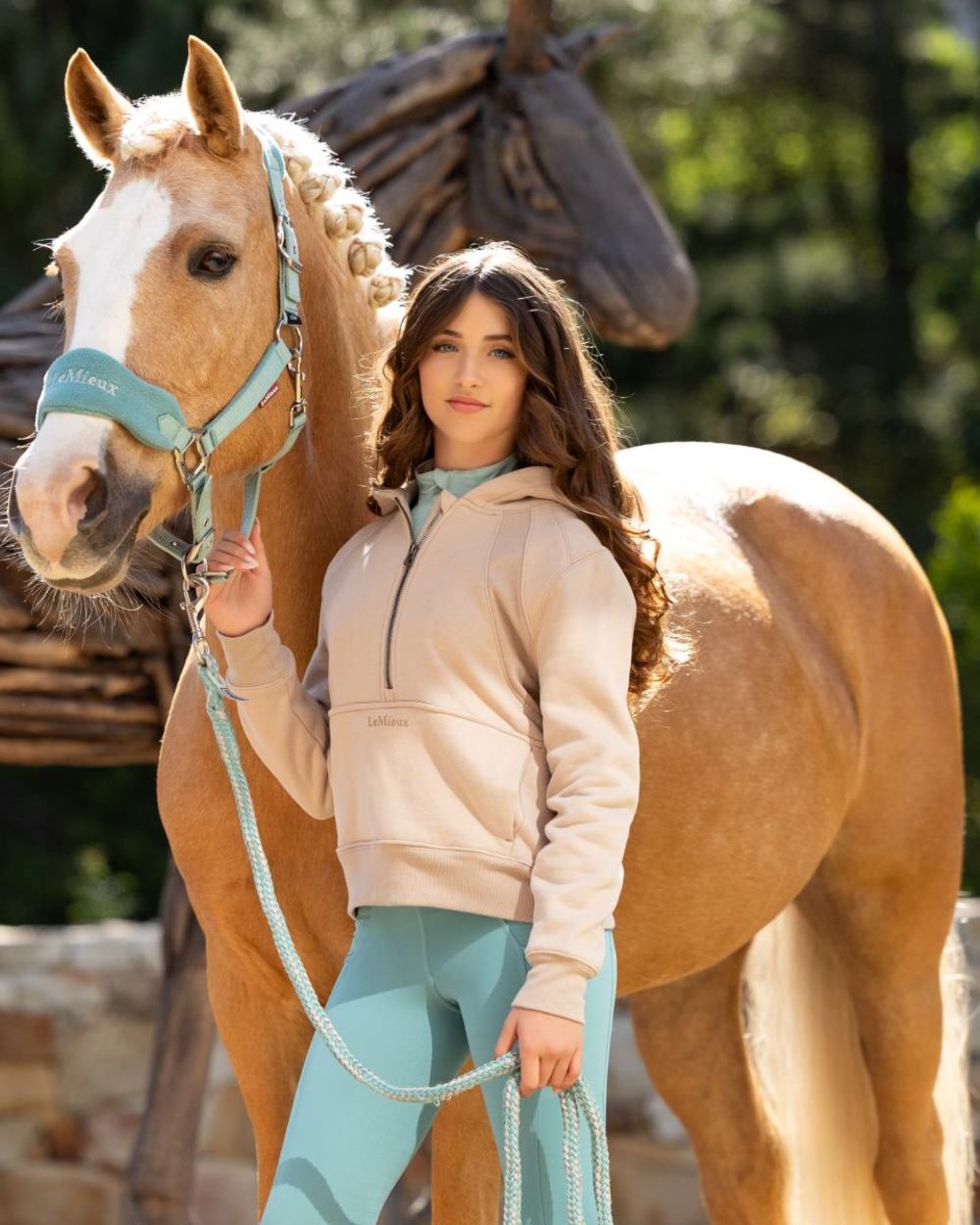 Almond coloured LeMieux Young Rider Harriet Pop Over Hoodie on blurry forest background