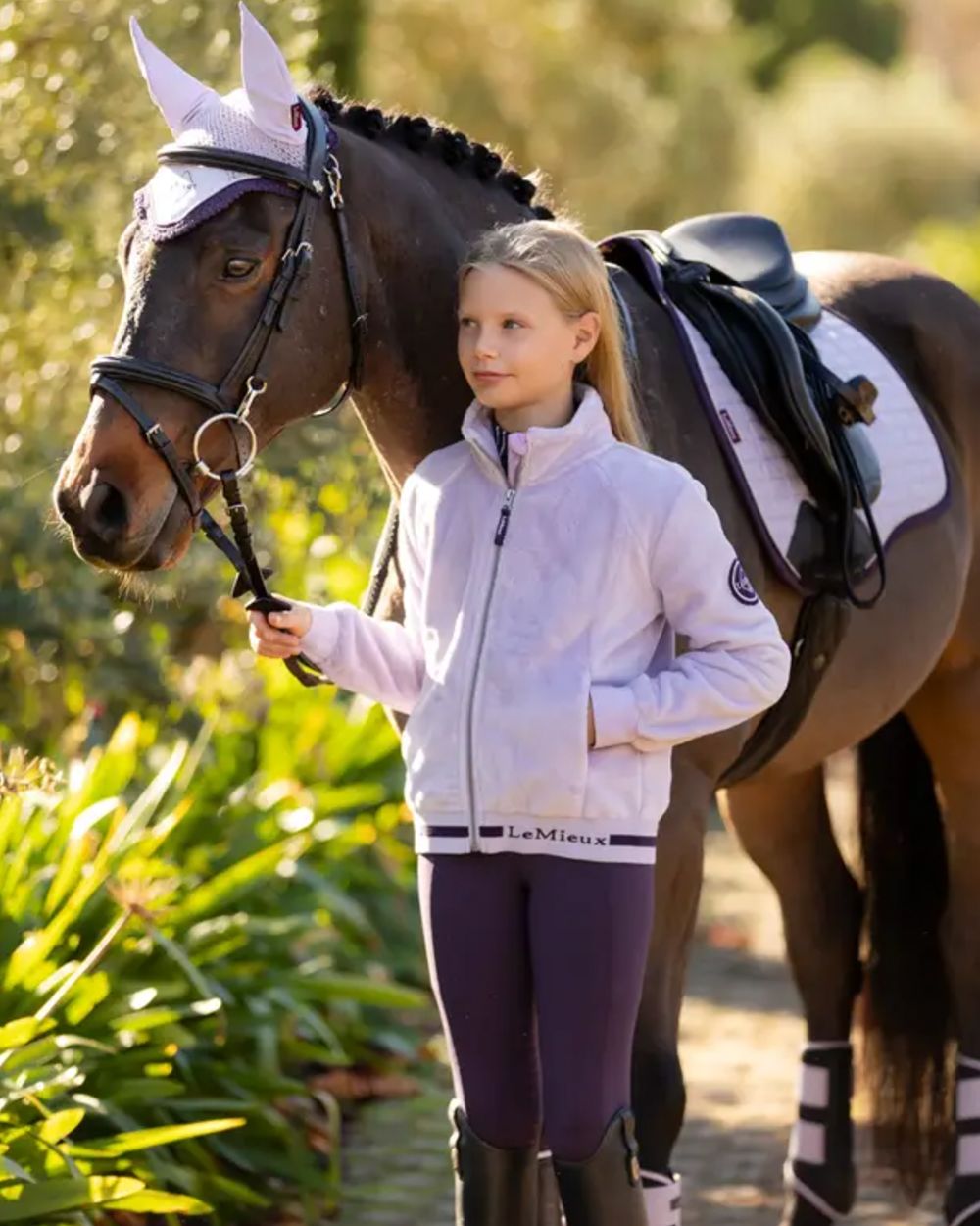 Lilac Coloured LeMieux Young Rider Libby Fleece Jacket On A Leafy Background