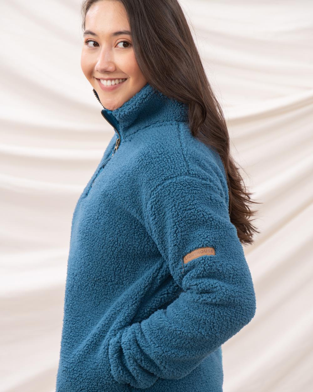 Teal coloured Lighthouse Ladies Coast Half Zip Fleece Sweater on curtain background