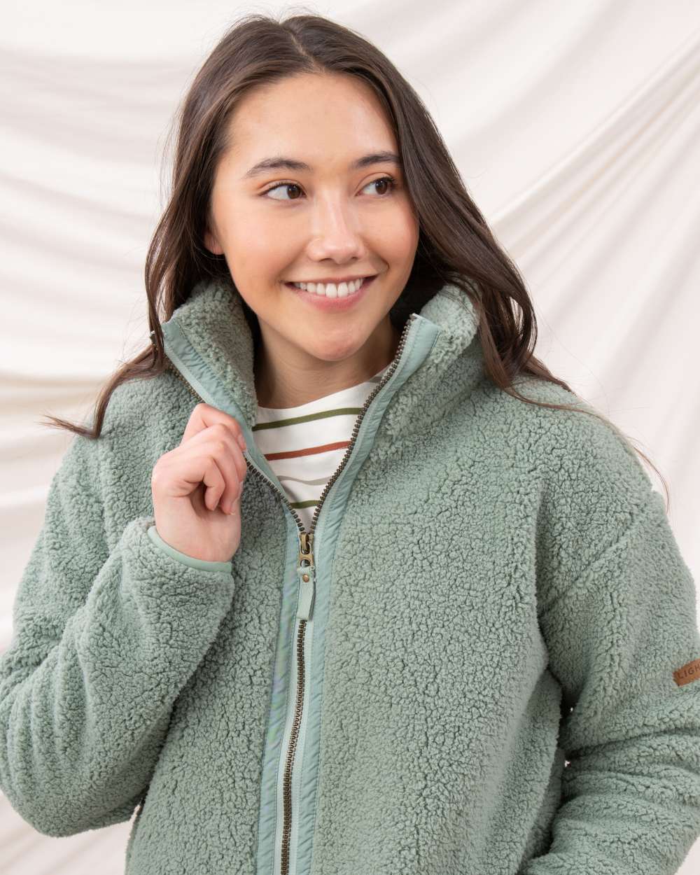 Sage coloured Lighthouse Ladies Cobh Full Zip Fleece Jacket on curtain background