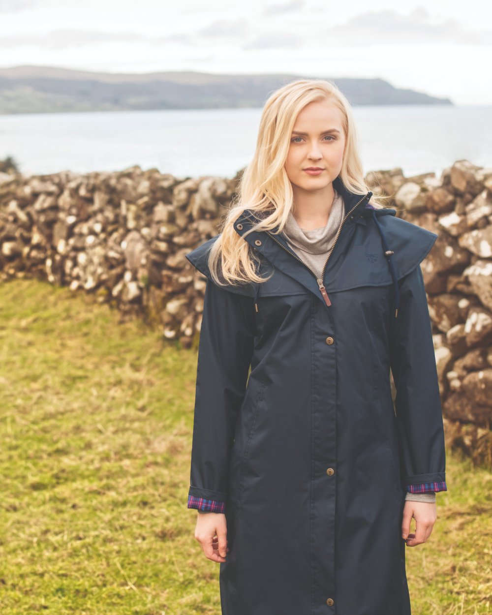 Nightshade coloured Lighthouse Outback Full Length Ladies Waterproof Raincoat on Stone Wall background