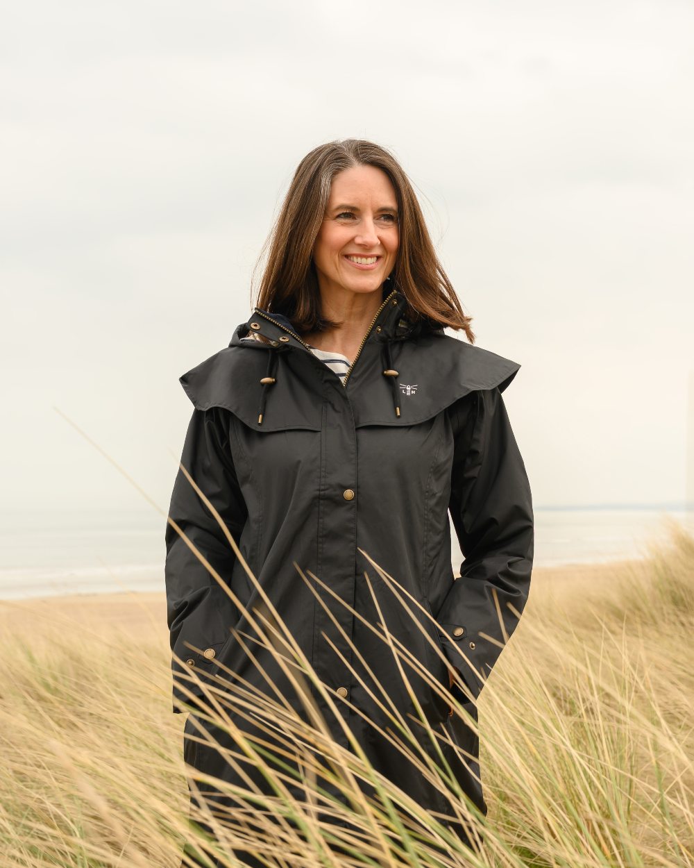 Black coloured Lighthouse Outback Full Length Ladies Waterproof Raincoat on Beach background 