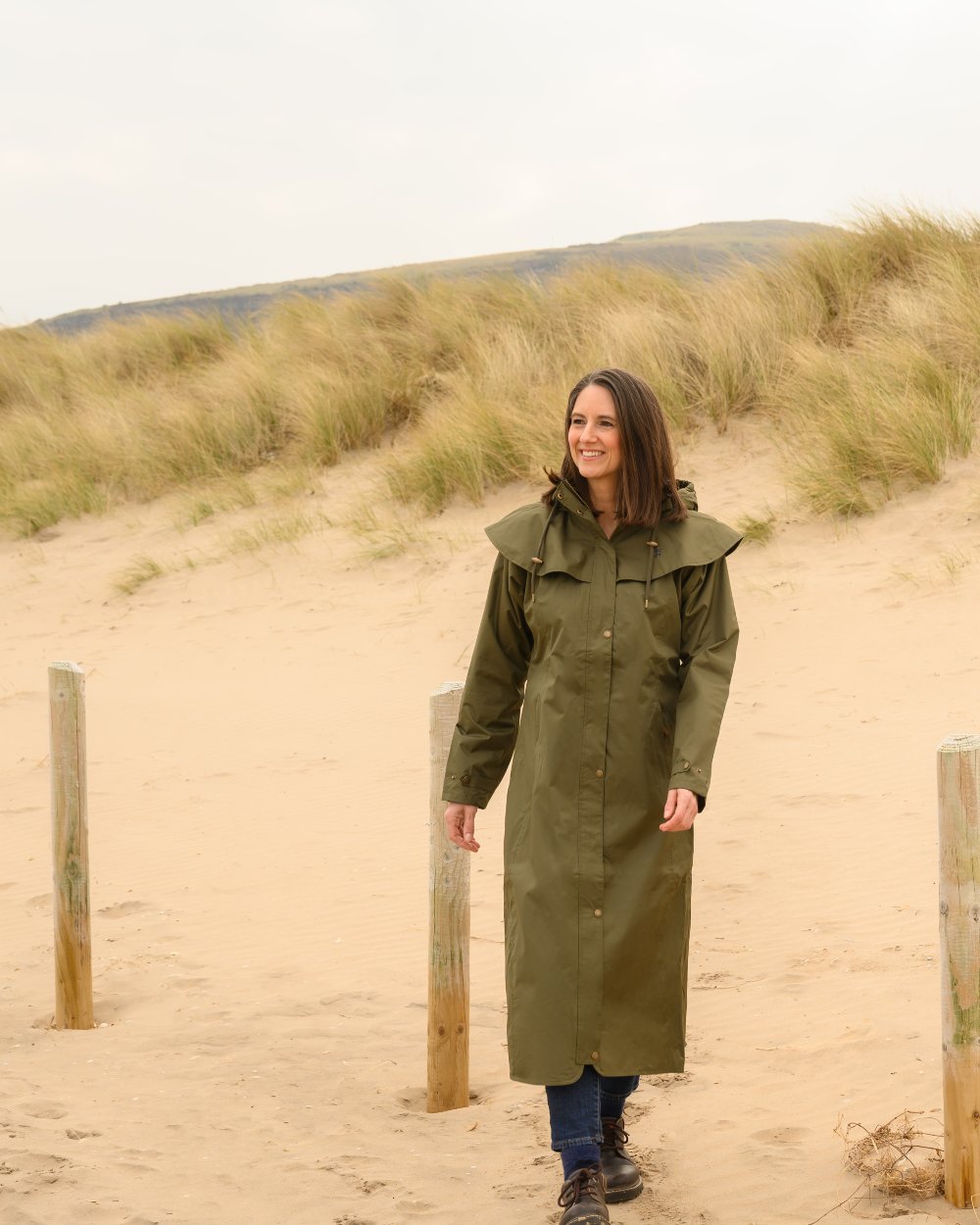 Fern coloured Lighthouse Outback Full Length Ladies Waterproof Raincoat on Beach background 