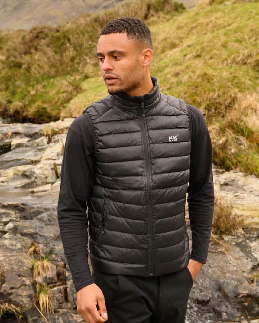 Jet Black coloured Mac In A Sac Mens Alpine Down Gilet on blurry mountain background