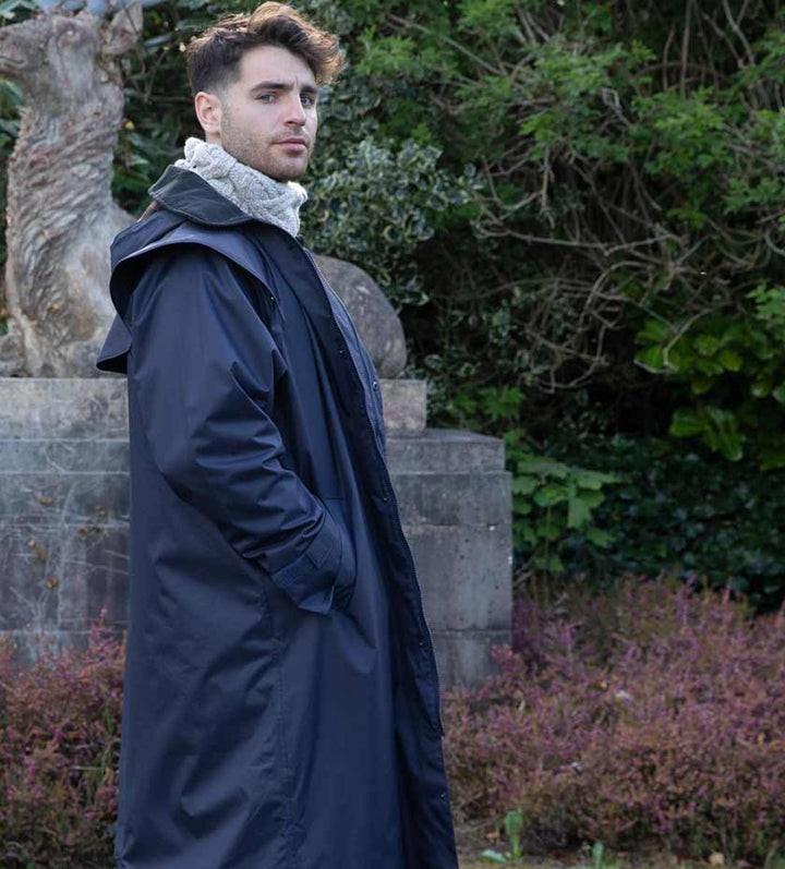 Men's Long Waterproof Coats. Man wears long rain mac with statue and trees in background.