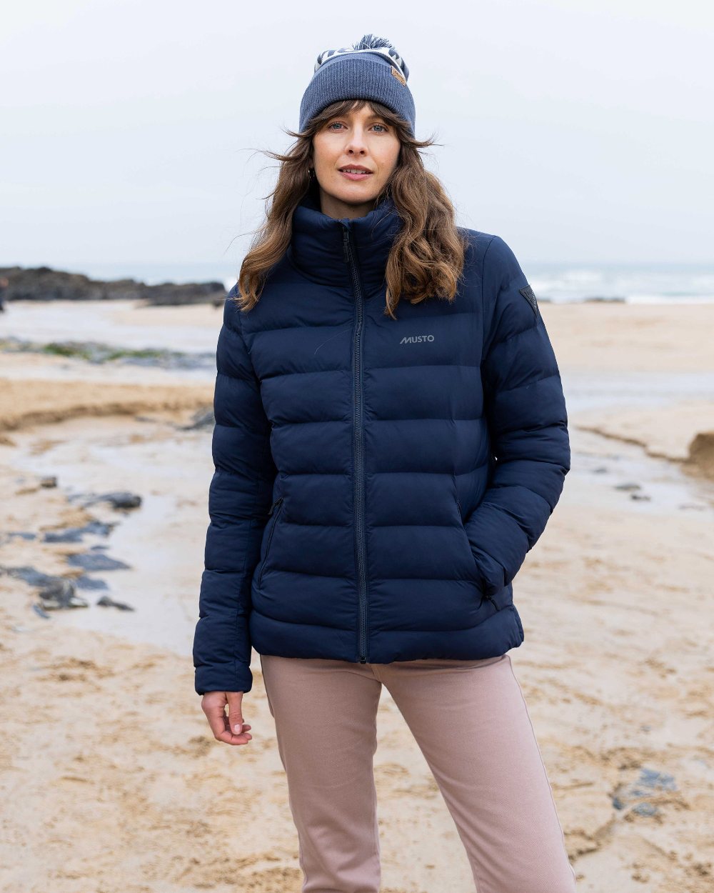 Ombre Blue Coloured Musto Bobble Hat on beach background