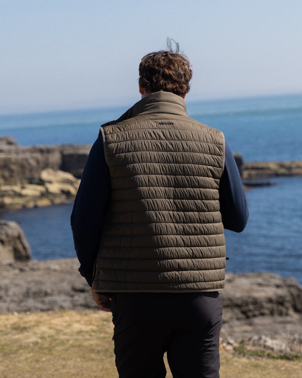 Crocodile Coloured Musto Mens Original Lite Puffer Vest on sea background