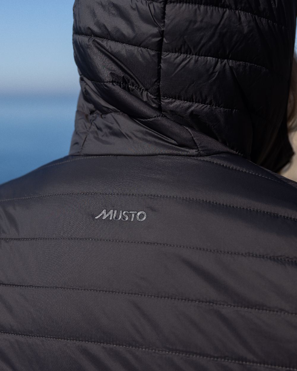 Carbon Coloured Musto Womens Original Lite Puffer Coat on sea background