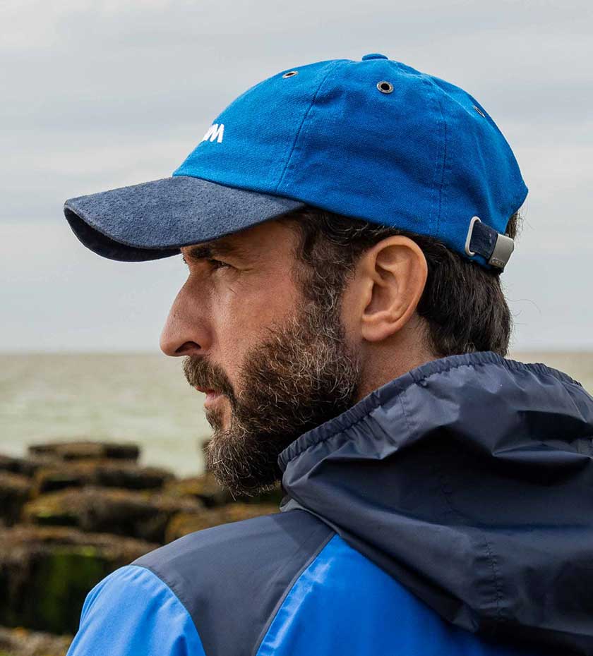 Man's Musto Sailing cap in Blue in sea in background.
