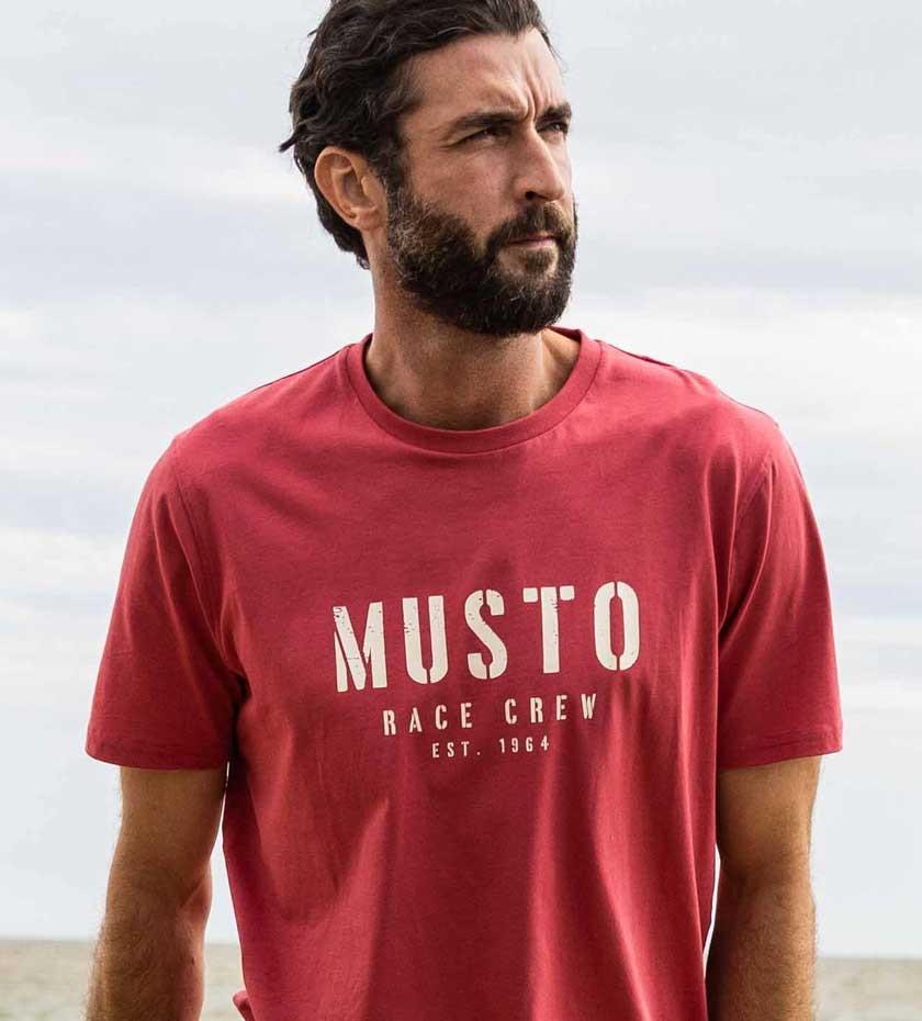 Man in Pink coloured MUSTO Race Sailing Crew logo T-shirt.