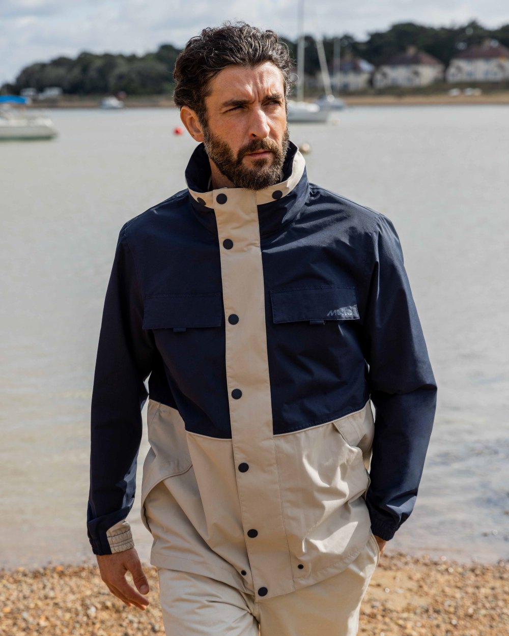 Pumice/Navy Coloured Musto Mens Classic Shore Waterproof Jacket On A Beach Background 