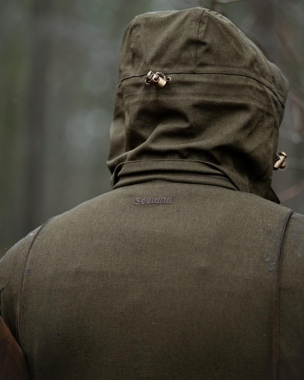 Shaded Olive coloured Seeland Mens Woodcock Royale Jacket on forest background