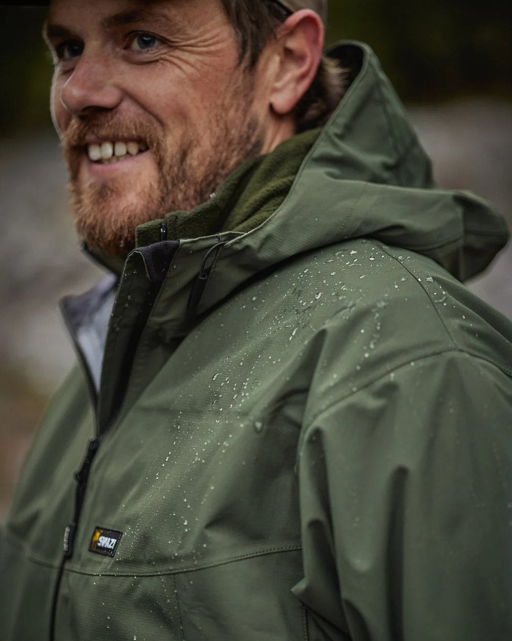 Olive coloured Swazi Mens Sentinel Ultralight Jacket on rock background