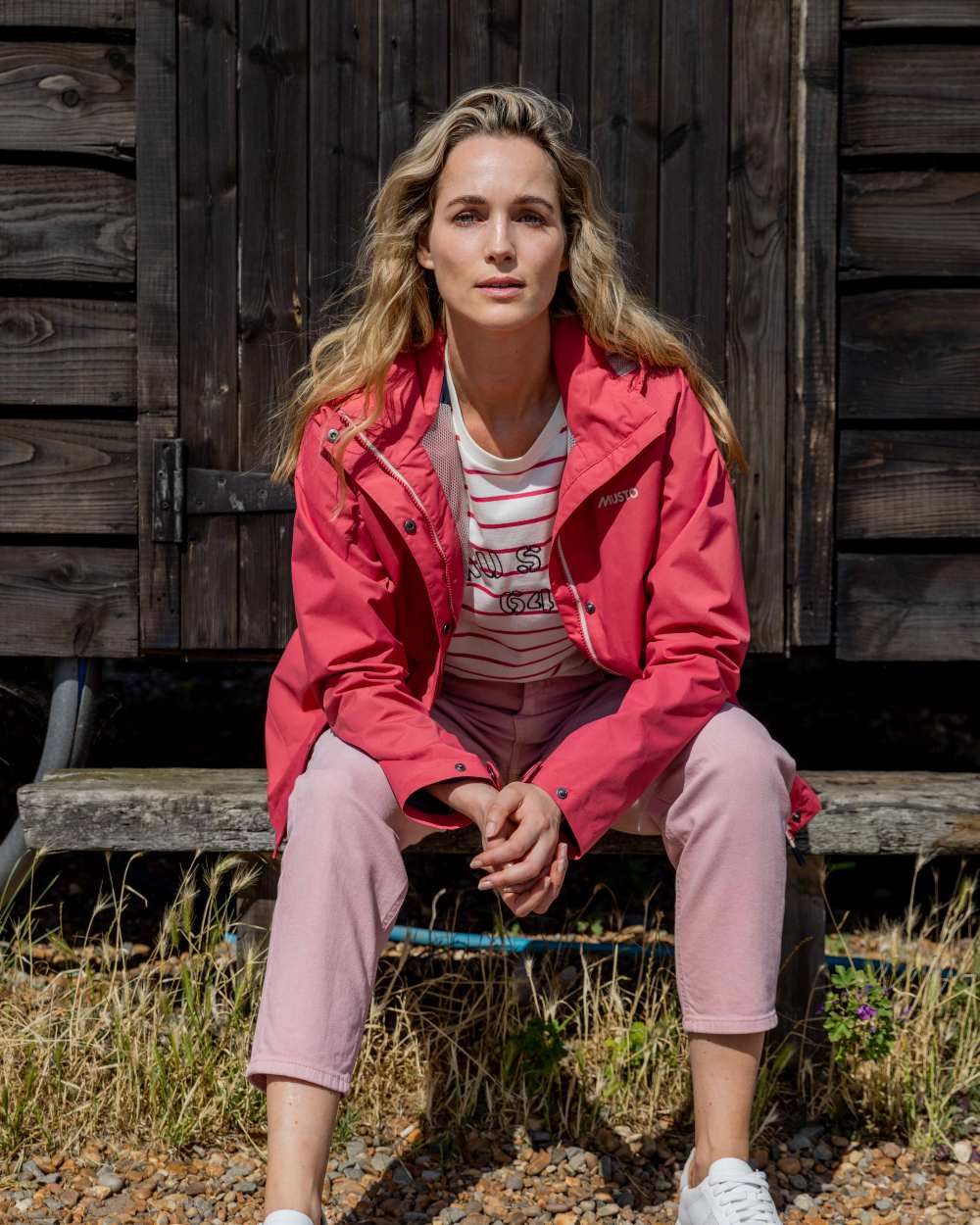 Sweet Raspberry Coloured Musto Womens Classic Shore Waterproof Jacket On A Coastal Background