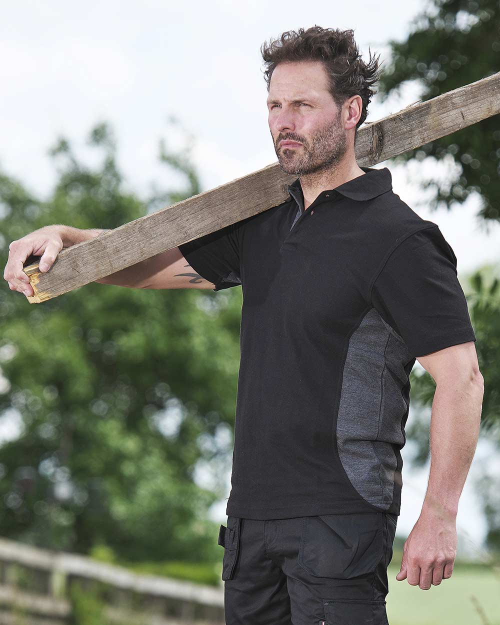 Black Coloured TuffStuff Pro Work Polo Shirt On A Garden Background