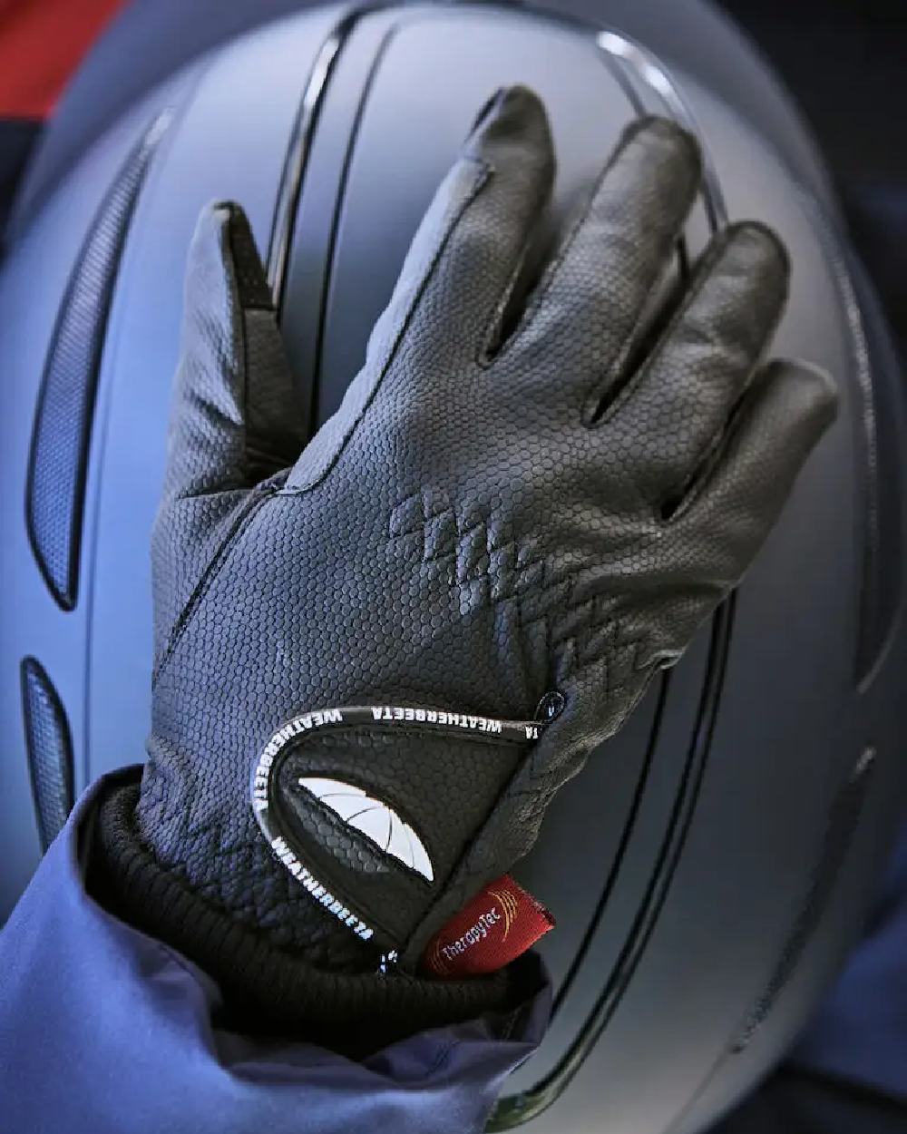 Black coloured WeatherBeeta Therapy-Tec Riding Gloves on helmet background