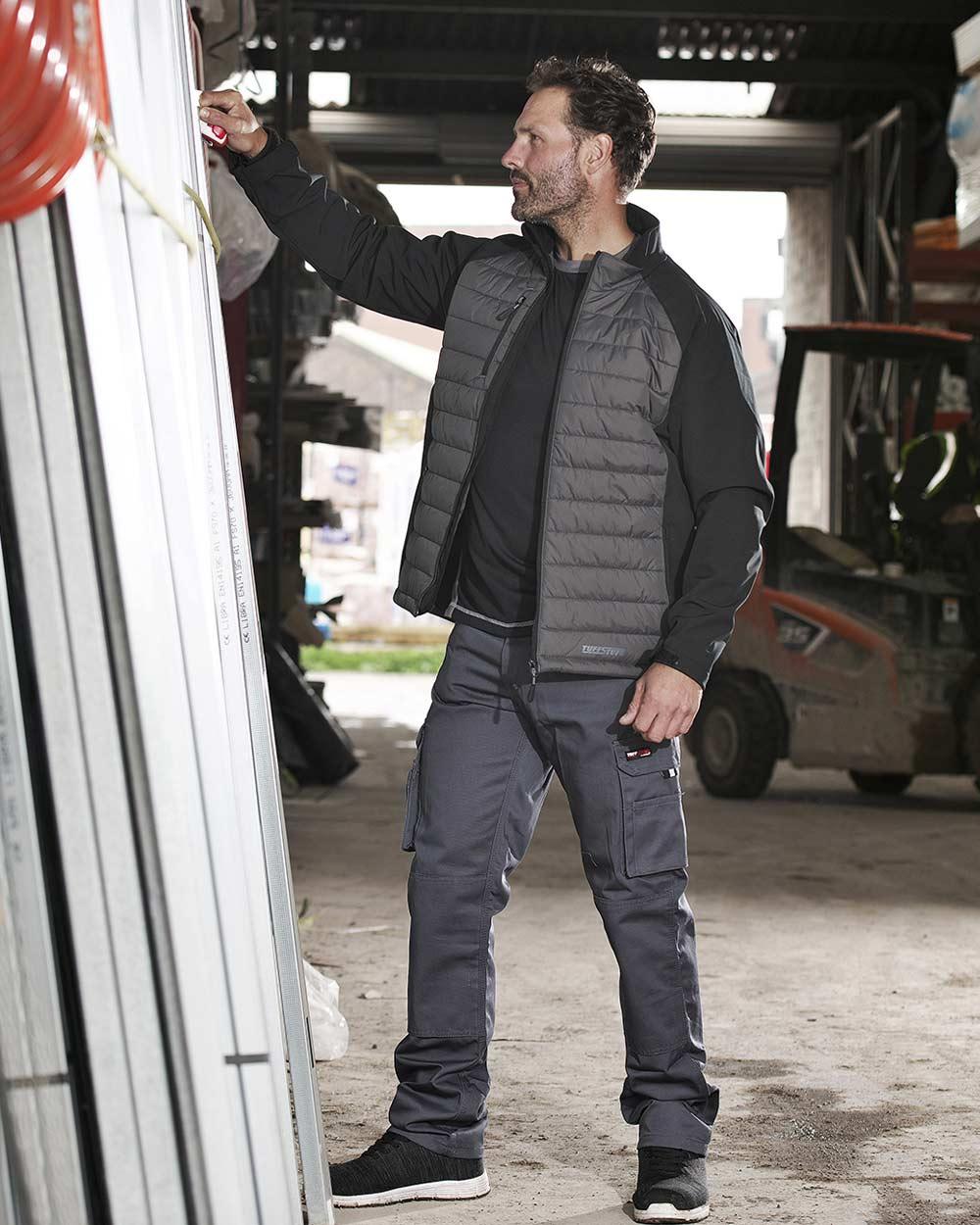 Grey Coloured TuffStuff Pro Work Trousers On A Warehouse Background