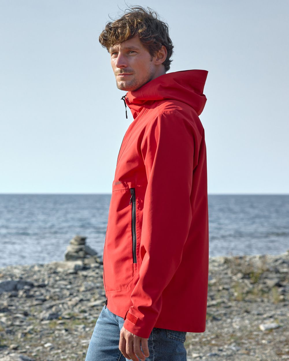 Pomme Red Coloured Didriksons Basil Unisex Waterproof Jacket 4 on Beach Background