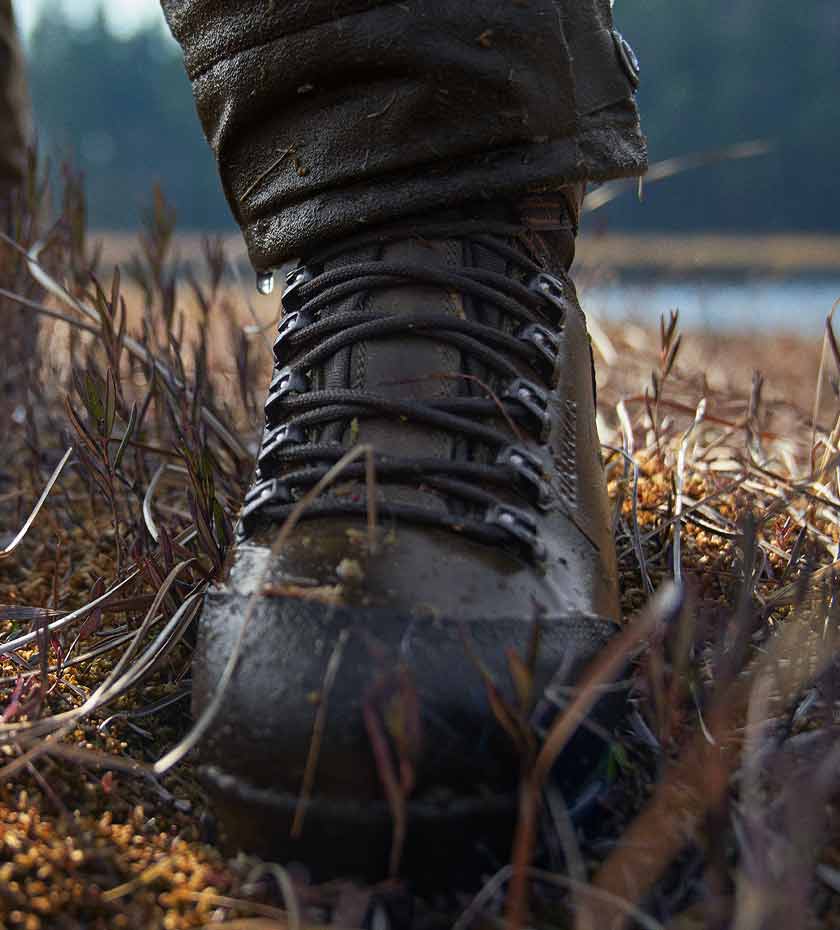 Harkila Hunting boot with laces splattered with mud and water on rough field background.