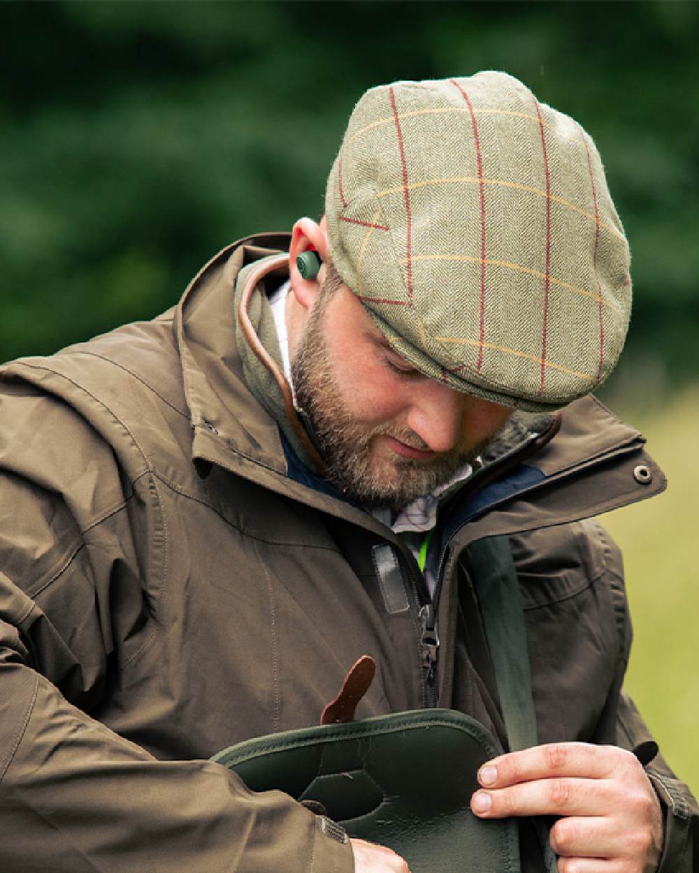 Tweed Green Coloured Jack Pyke Wool Blend Tweed Flat Cap On A Blurry Background