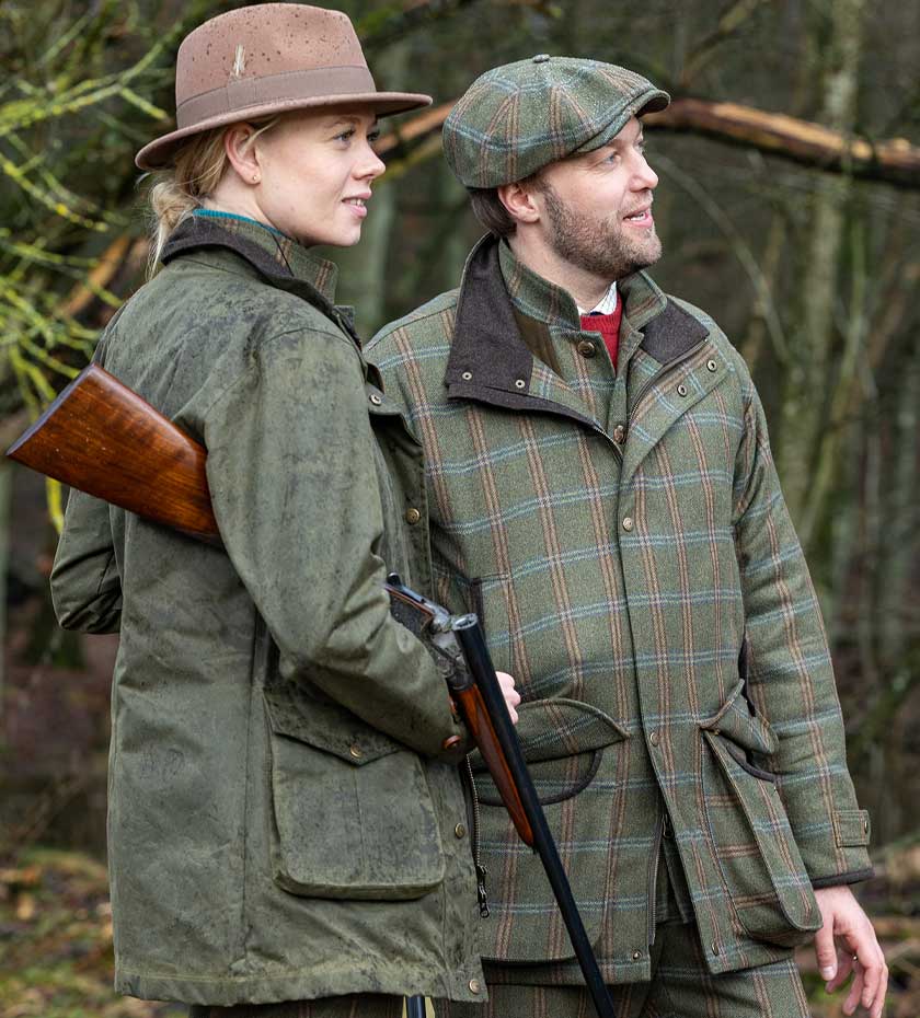 Laksen Jackets & smocks | a man and a woman wearing a tweed shooting jacket and a wax cotton jacket with a wooded area in background.