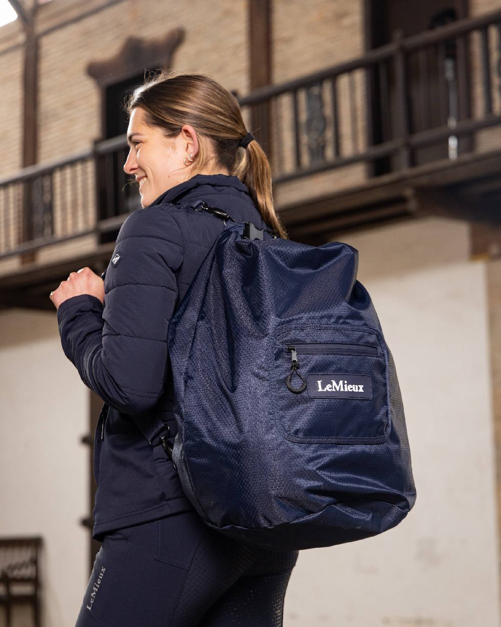 Navy coloured LeMieux Carry All Backpack with blurry building in background 