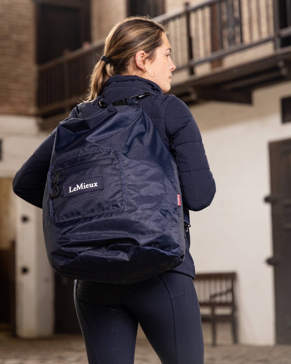 Navy coloured LeMieux Carry All Backpack with blurry building in background 