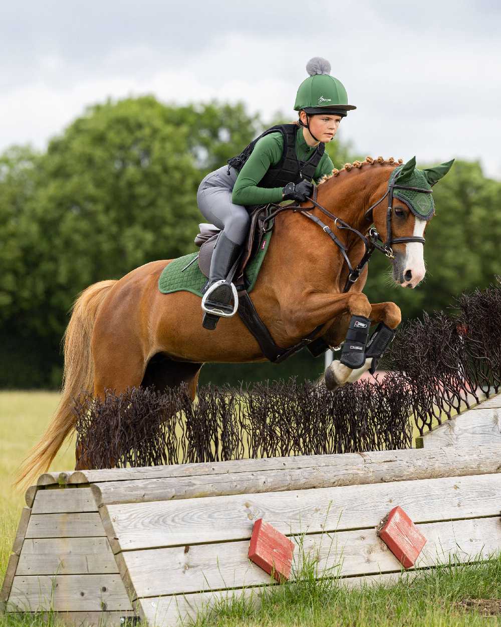 Hunter Green coloured LeMieux Young Rider Base Layer with trees in background